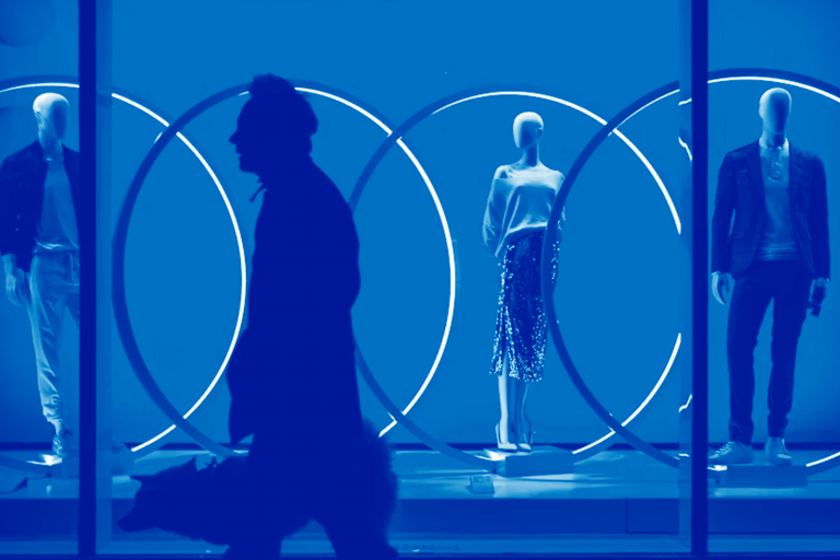 Silhueta de pessoa caminhando em frente a vitrine com manequins futuristas iluminados por círculos de neon azul, representando o design de negócios centrado no cliente